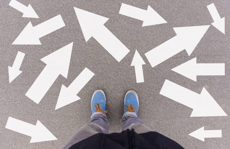 Confusing direction arrows on asphalt ground, feet and shoes on floor, personal orientation concept