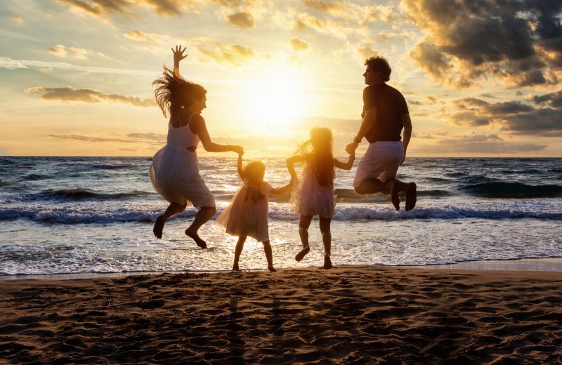 Glückliche Familie im Urlaub springt vor Freude am Strand währ