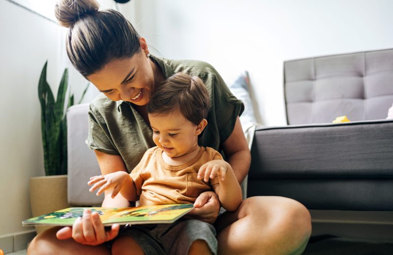 Mom reading a book with baby boy at home. Early age children education, development. Mother and child spending time together. Candid lifestyle.